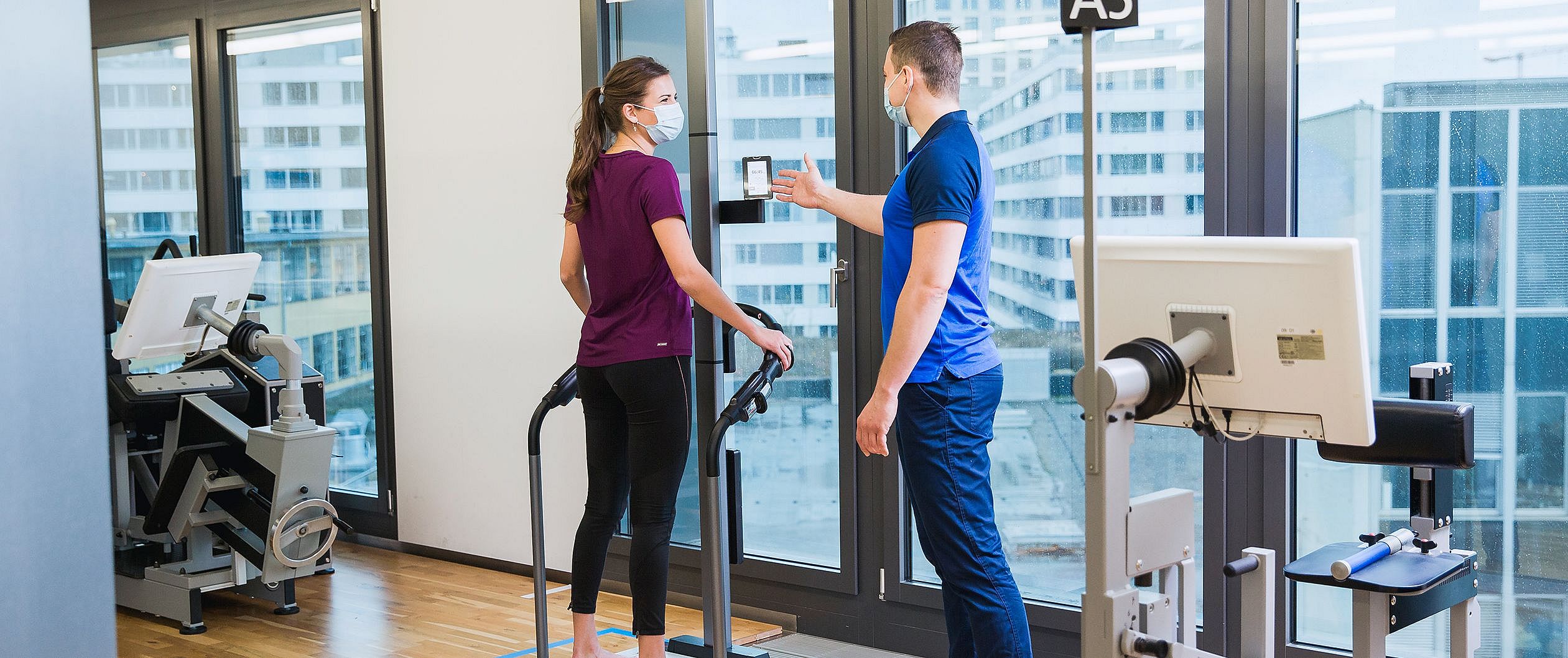 BIA Messung | Kieser Das Bild zeigt einen Kieser-Kunden, der von einem Trainer bei einer BIA-Messung begleitet wird. Die BIA ist eine Körperwaage, die Muskel- und Fettmasse misst.